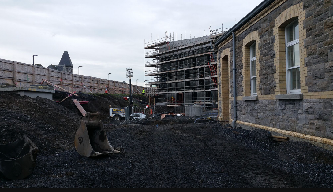 Excavator bucket and scaffolding beside historic stone building construction site